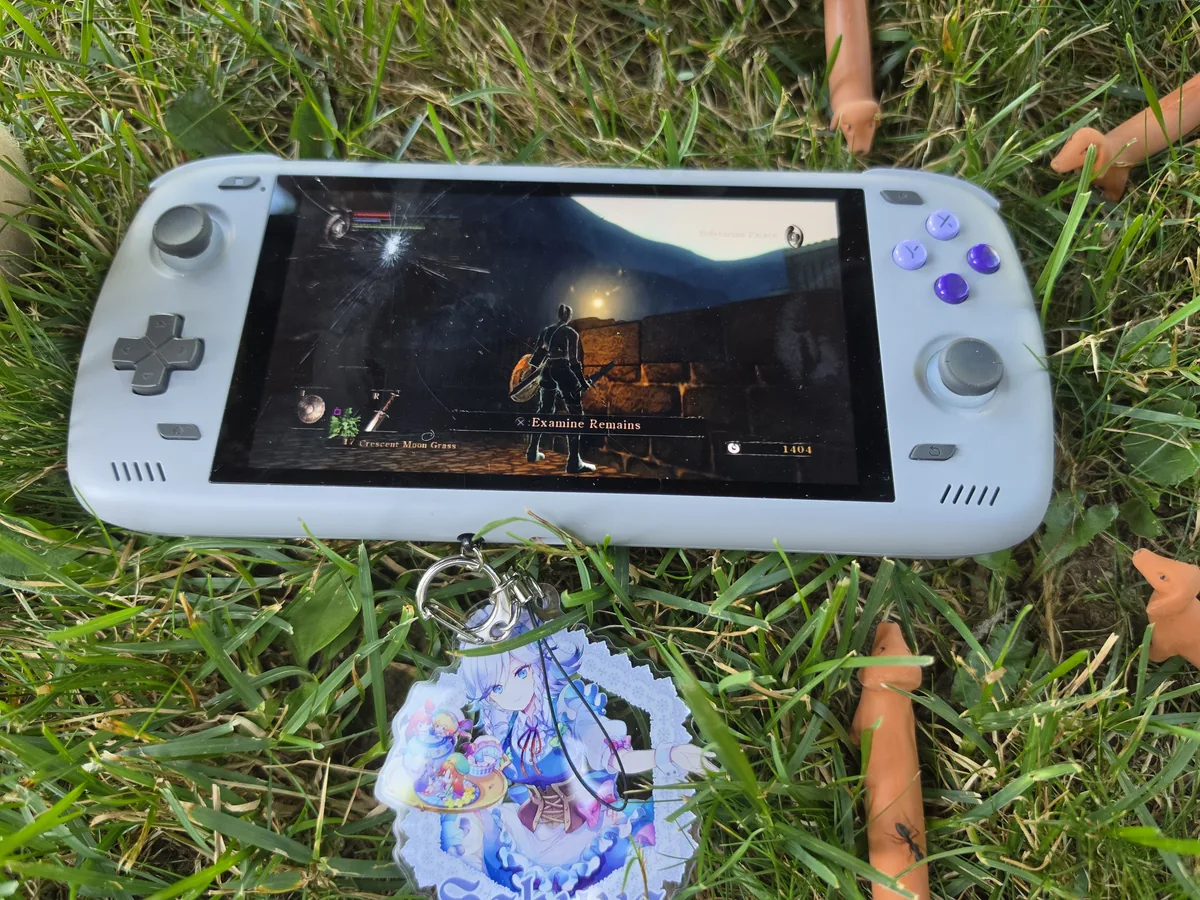 An Odin 2 with a cracked screen lying in the grass among thumbnail props